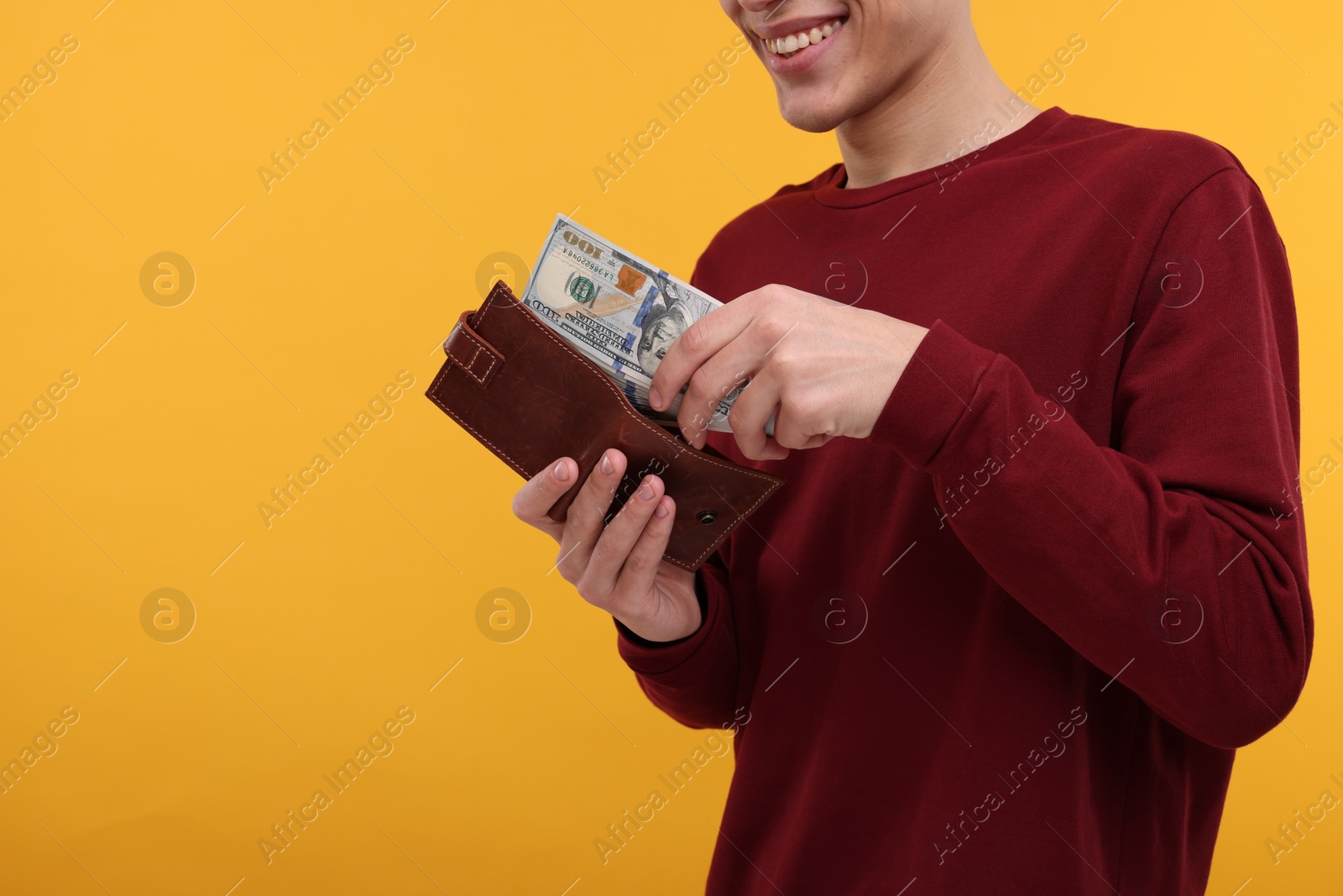 Photo of Happy man putting money into wallet on yellow background, closeup. Space for text