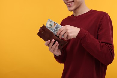 Happy man putting money into wallet on yellow background, closeup. Space for text