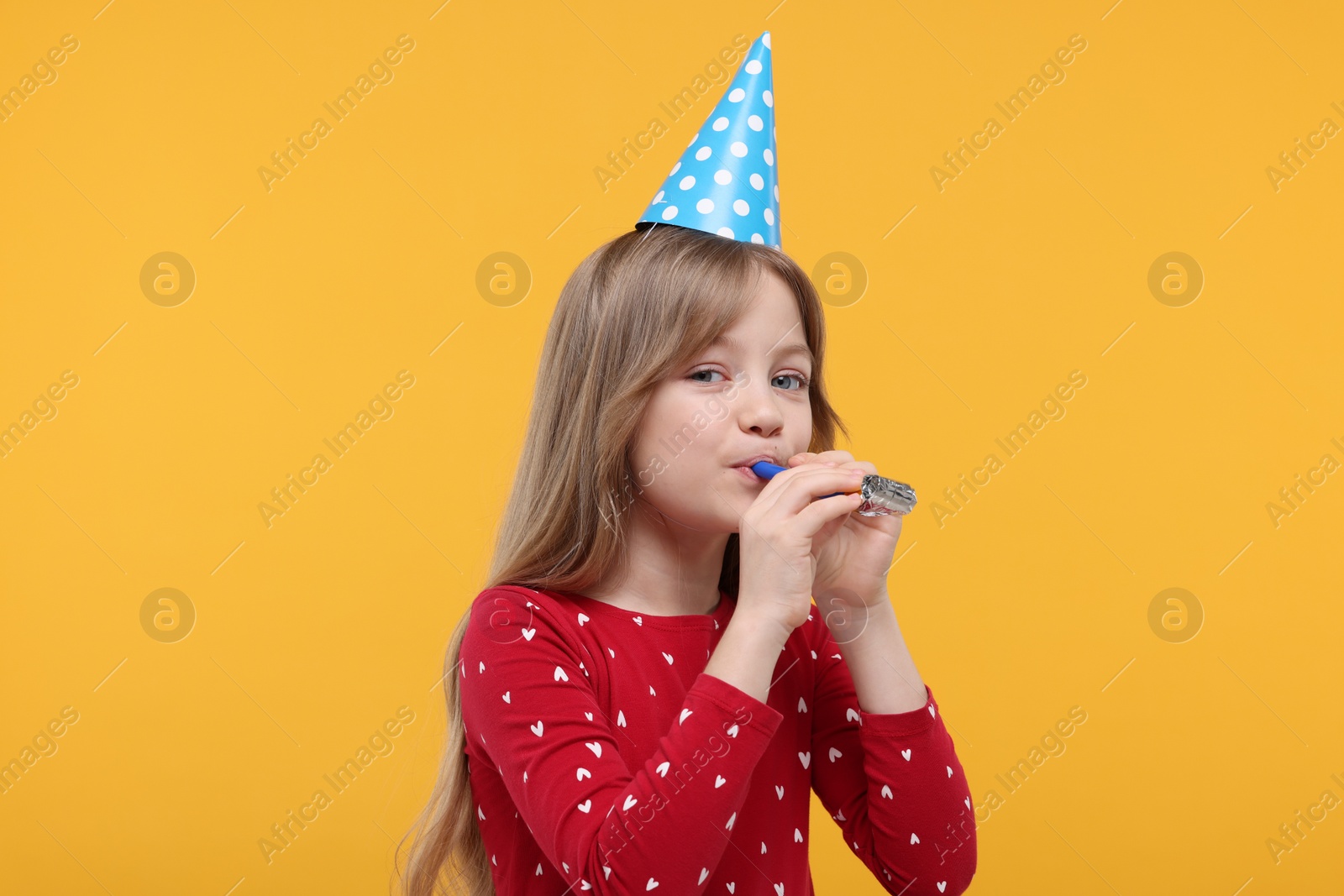 Photo of Cute little girl in party hat with blower on yellow background