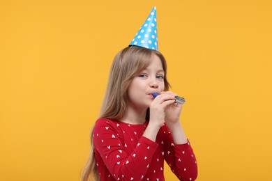 Photo of Cute little girl in party hat with blower on yellow background