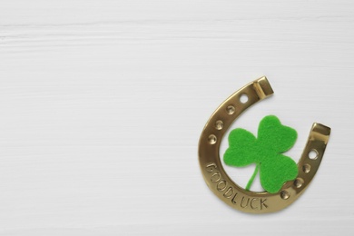Photo of Decorative clover leaf and horseshoe on white wooden background, flat lay with space for text. St. Patrick's Day celebration