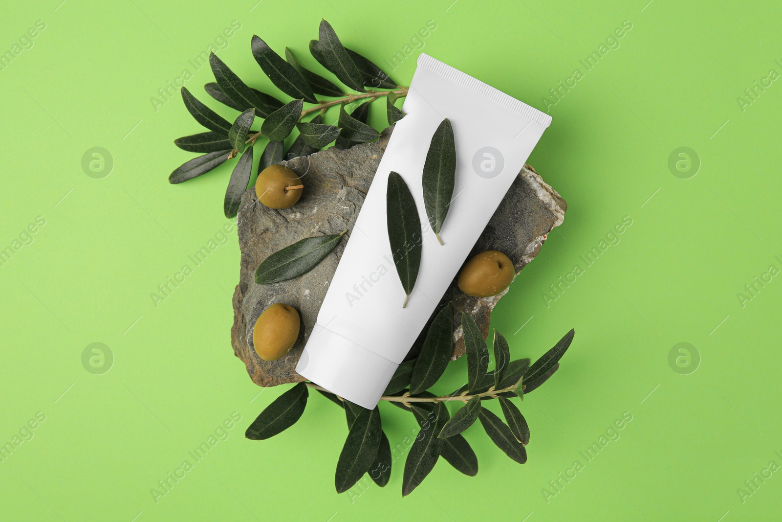 Photo of Tube of cream and olives on light green background, flat lay