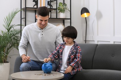 Photo of Little boy with his father putting coin into piggy bank at home