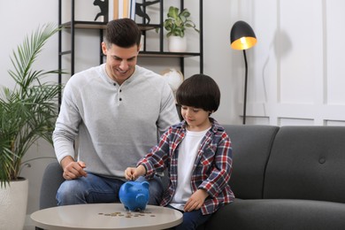 Little boy with his father putting coin into piggy bank at home