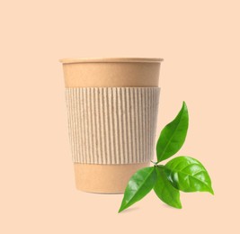 Image of Takeaway paper coffee cup with cardboard sleeve and green leaves on beige background. Eco friendly lifestyle