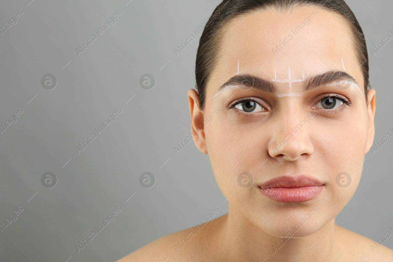 Photo of Eyebrow correction. Young woman with markings on face against grey background, space for text