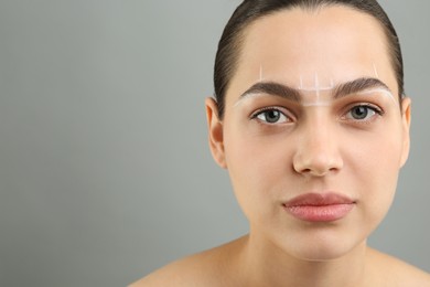 Photo of Eyebrow correction. Young woman with markings on face against grey background, space for text