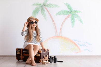 Adorable little child playing traveler with suitcase indoors