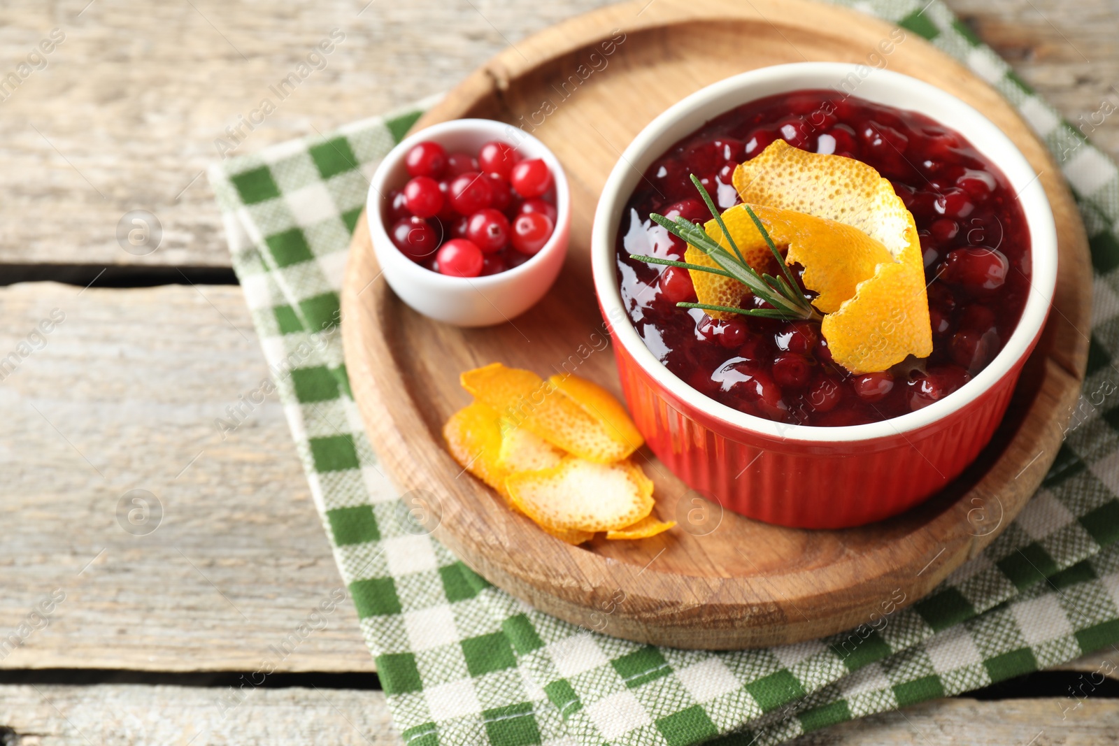 Photo of Cranberry sauce in bowl, fresh berries, rosemary and orange peels on wooden table, space for text