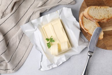 Photo of Tasty butter with curls, slices of bread and knife on light grey table, flat lay
