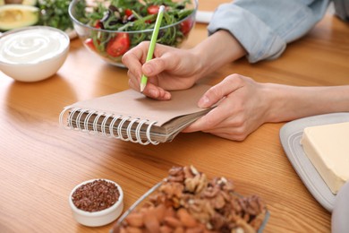 Woman with notebook and different products at wooden table, closeup. Keto diet