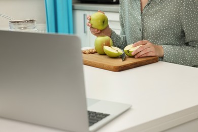 Woman making apple cake while watching online cooking course via laptop in kitchen, closeup. Time for hobby