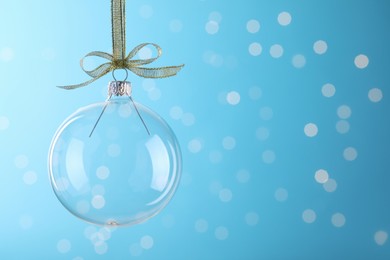 Photo of Transparent glass Christmas ball with golden ribbon and bow against light blue background. Space for text