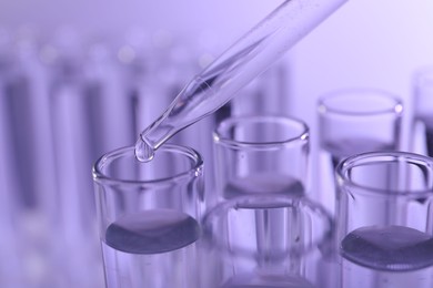 Dripping liquid from pipette into test tube on violet background, closeup