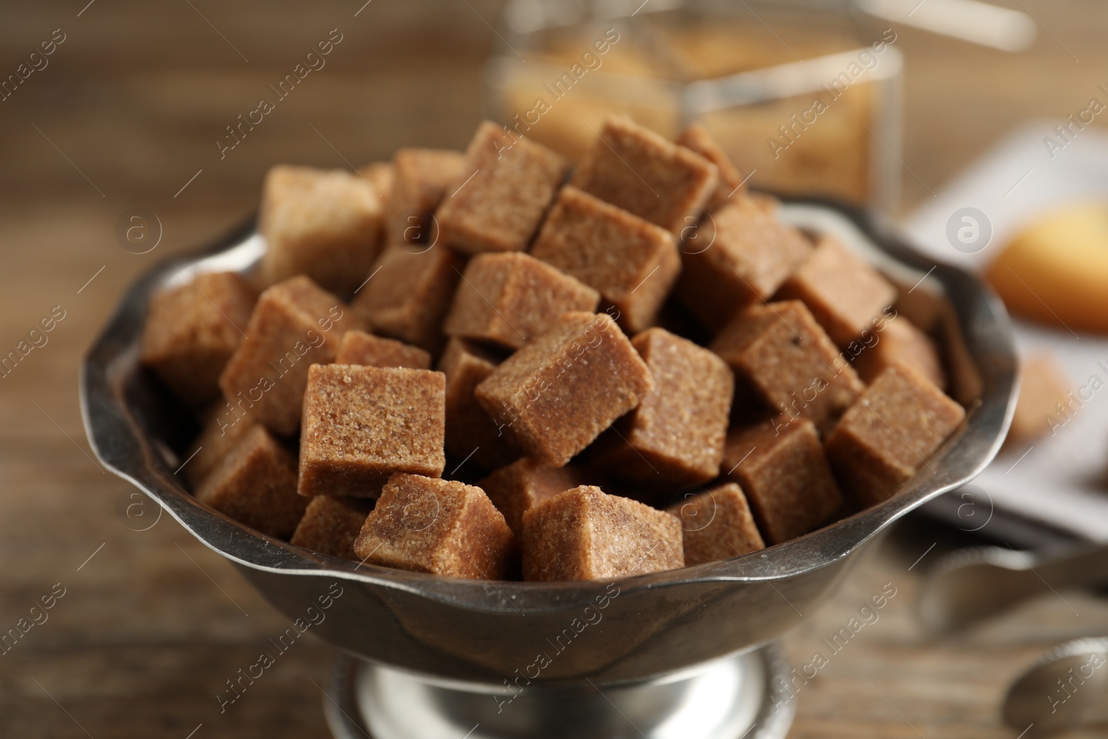 Photo of Brown sugar cubes in metal bowl on wooden table, closeup