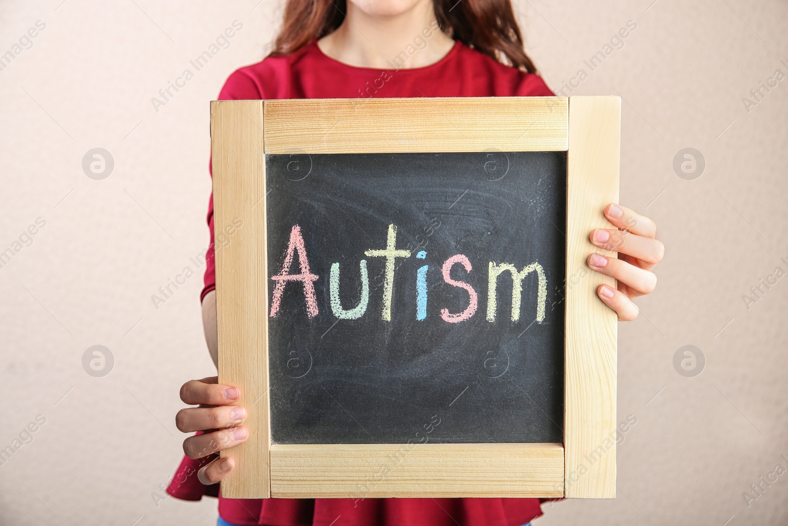 Photo of Woman holding chalkboard with word AUTISM on light background