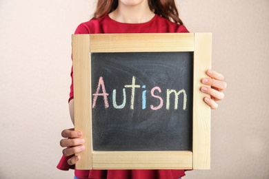 Photo of Woman holding chalkboard with word AUTISM on light background