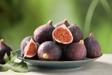 Plate with fresh ripe figs and green leaf on light table, closeup