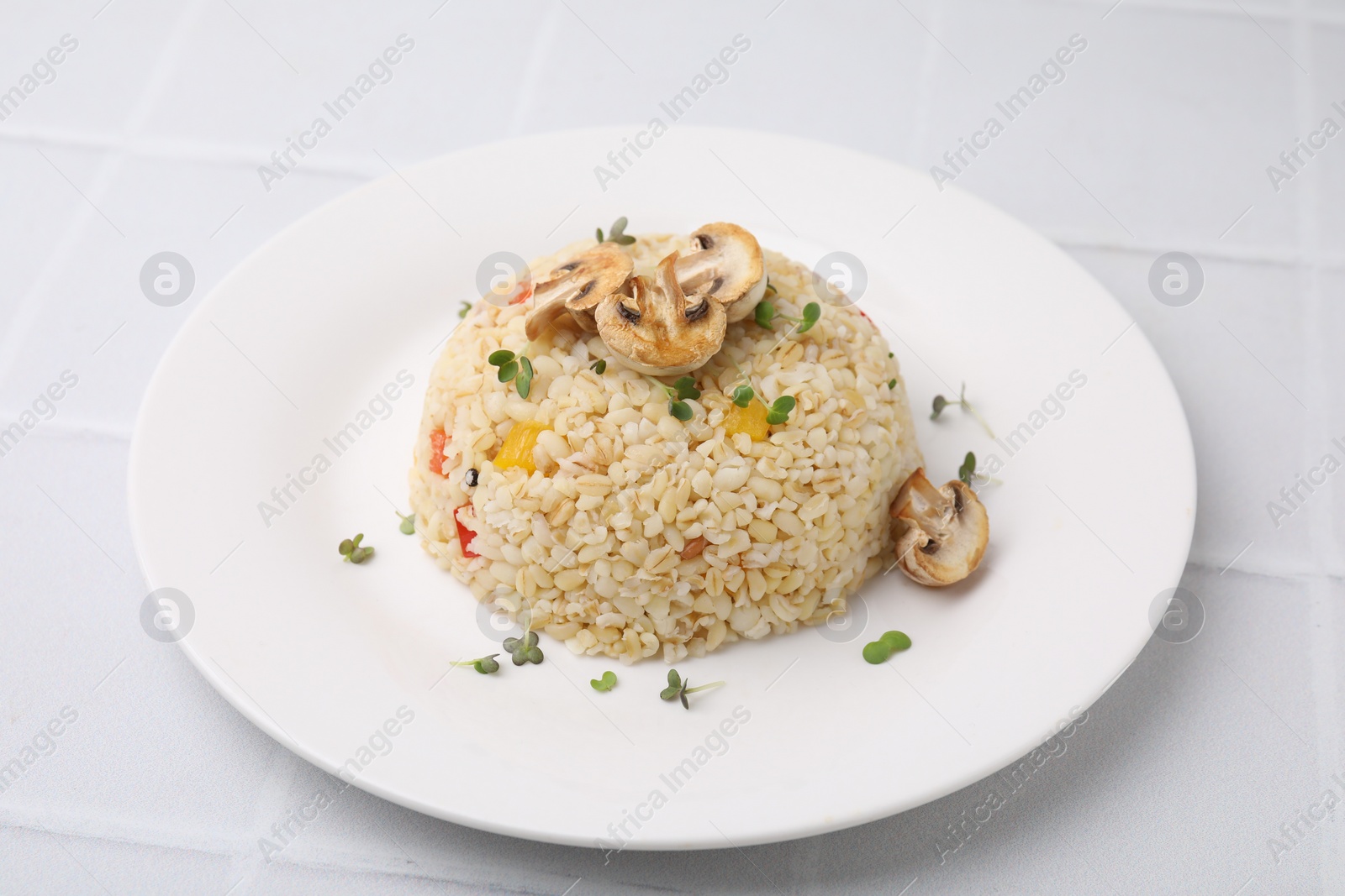 Photo of Delicious bulgur with vegetables, mushrooms and microgreens on white table, closeup