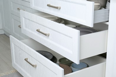 Open drawers with different plates and bowls in kitchen