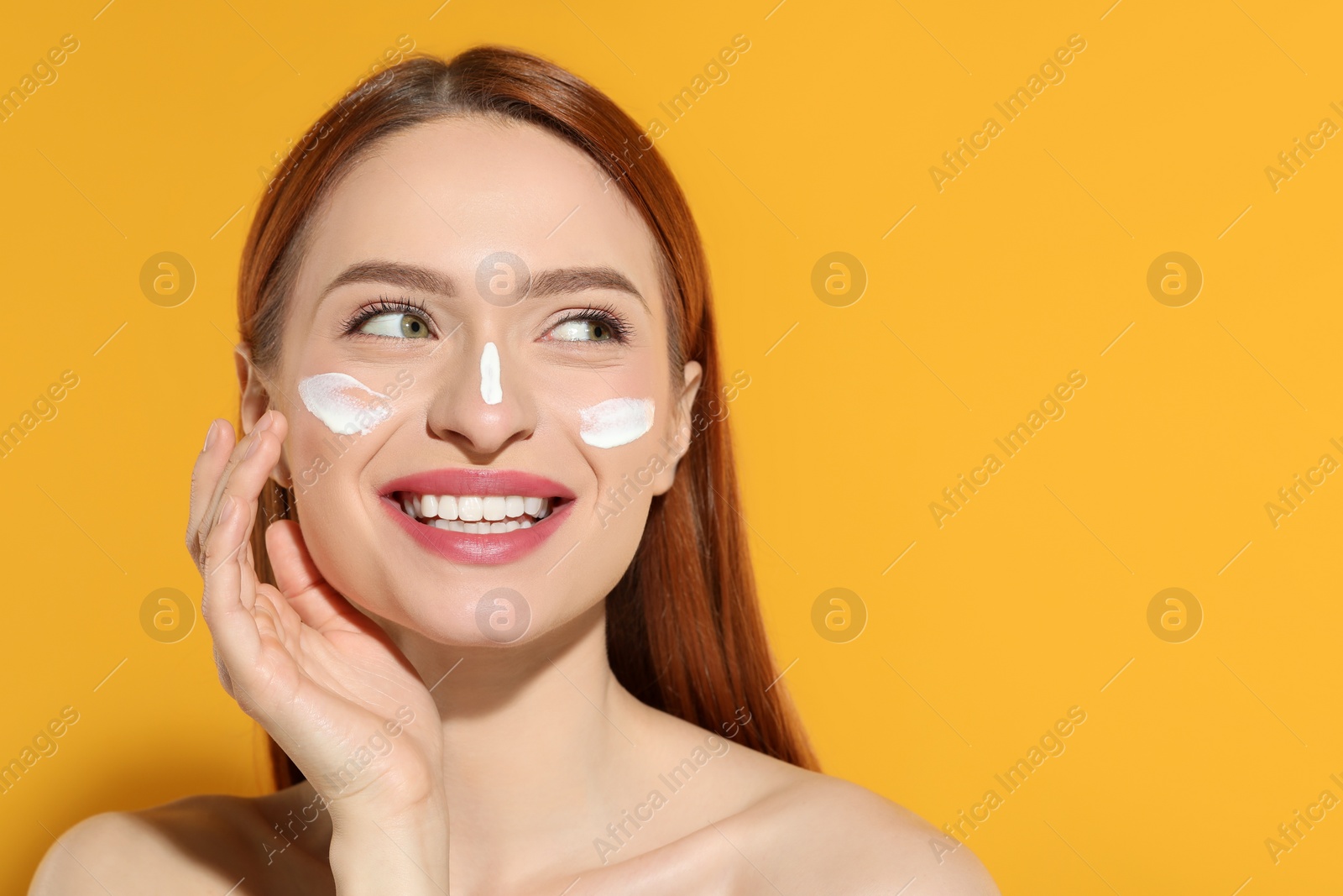 Photo of Beautiful young woman with sun protection cream on her face against orange background, space for text