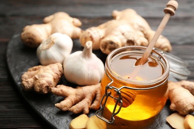 Photo of Ginger, honey and garlic on black table, closeup. Natural cold remedies