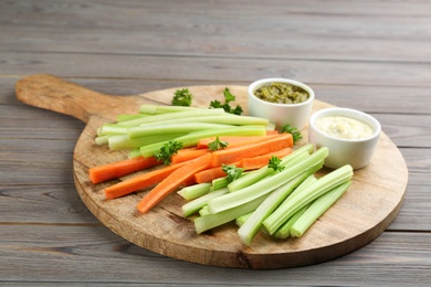 Celery and other vegetable sticks with different sauces on wooden table