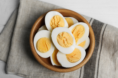Photo of Cut hard boiled chicken eggs in bowl on table, flat lay