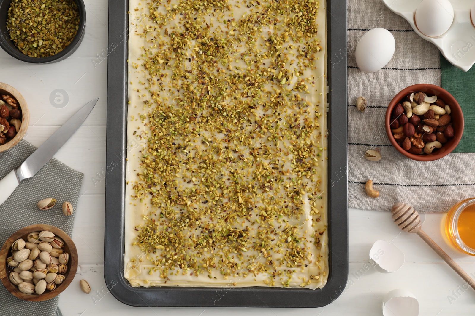 Photo of Making delicious baklava. Baking pan with dough and ingredients on white wooden table, flat lay