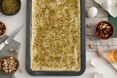 Making delicious baklava. Baking pan with dough and ingredients on white wooden table, flat lay