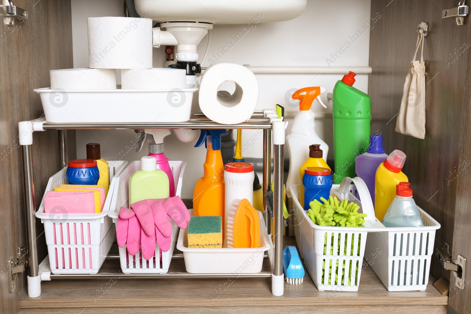 Photo of Open under sink cabinet with different cleaning supplies in kitchen