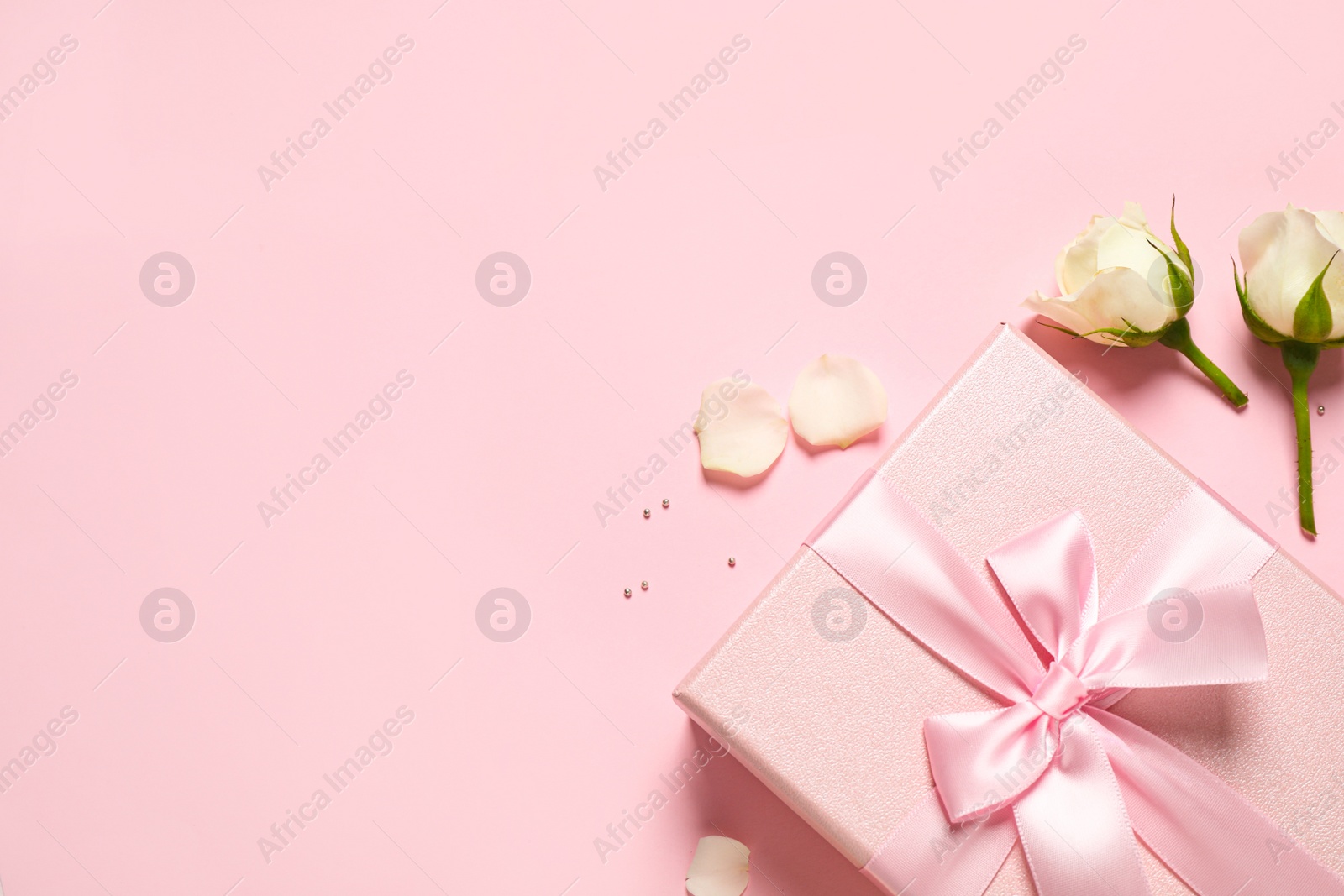 Photo of Elegant gift box and beautiful flowers on pink background, flat lay. Space for text