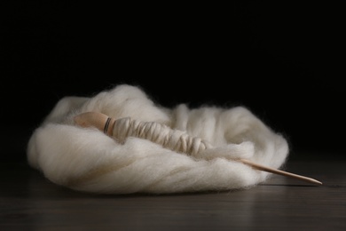 Photo of Soft white wool with spindle on wooden table against black background