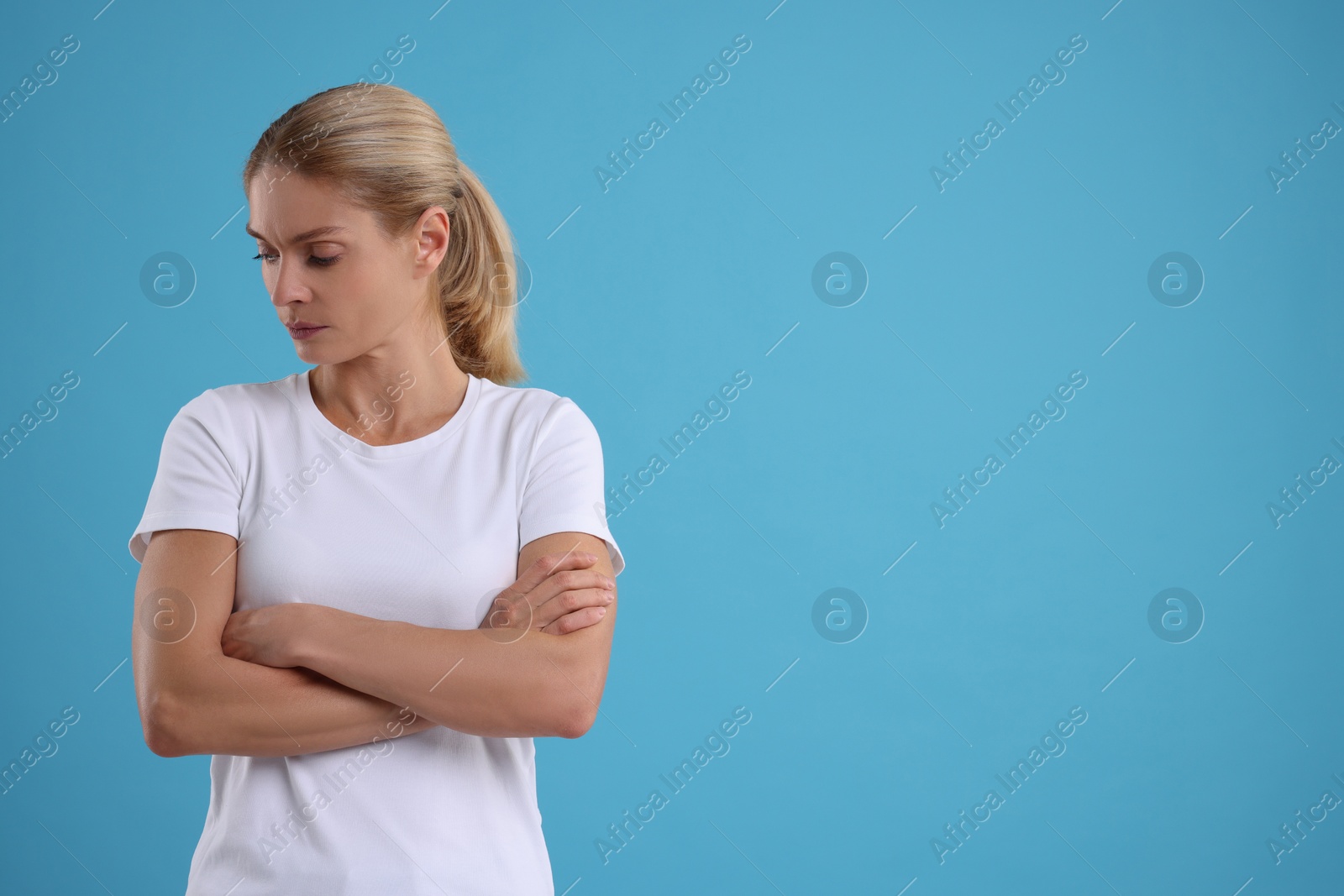 Photo of Resentful woman with crossed arms on light blue background. Space for text