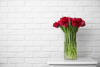 Photo of Bouquet of beautiful tulips in glass vase on white nightstand indoors. Space for text