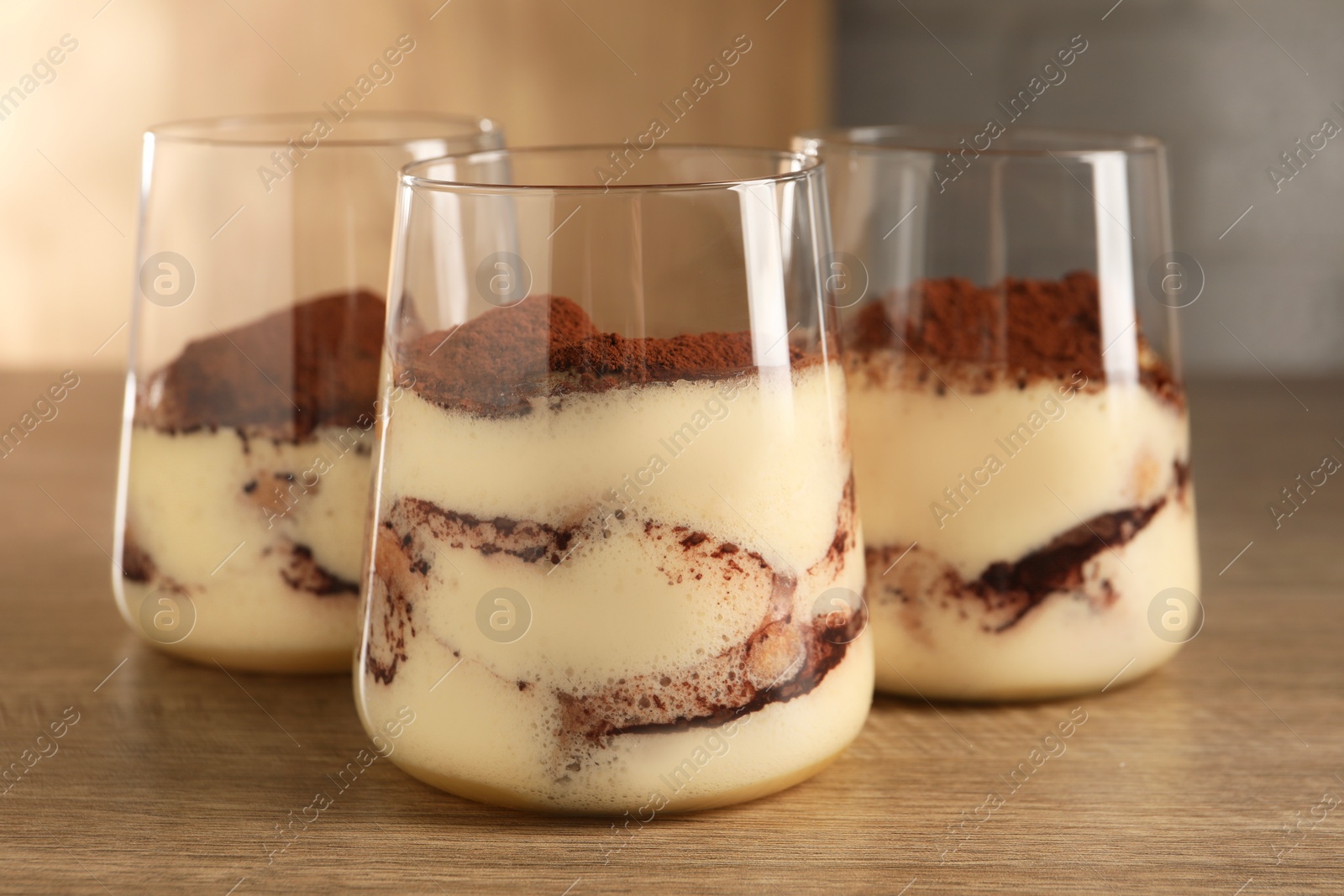 Photo of Delicious tiramisu in glasses on wooden table, closeup