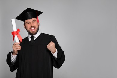 Photo of Emotional student with graduation hat and diploma on grey background. Space for text