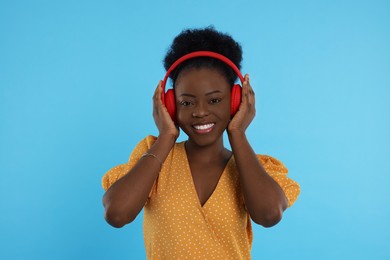 Photo of Beautiful young woman in headphones enjoying music on light blue background
