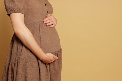 Photo of Pregnant woman in dress on light brown background, closeup. Space for text