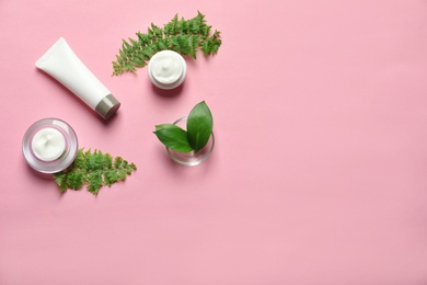Photo of Different skin care cosmetic products with green leaves on color background, top view