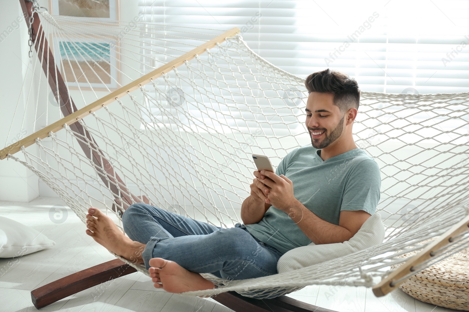 Photo of Young man using smartphone in hammock at home