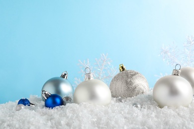 Photo of Christmas tree decoration on artificial snow against light blue background. Space for text