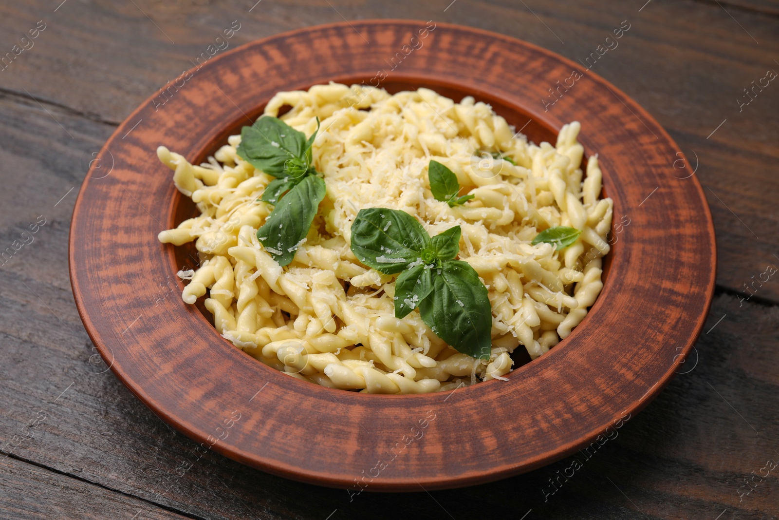 Photo of Plate of delicious trofie pasta with cheese and basil leaves on wooden table