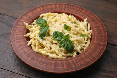 Plate of delicious trofie pasta with cheese and basil leaves on wooden table