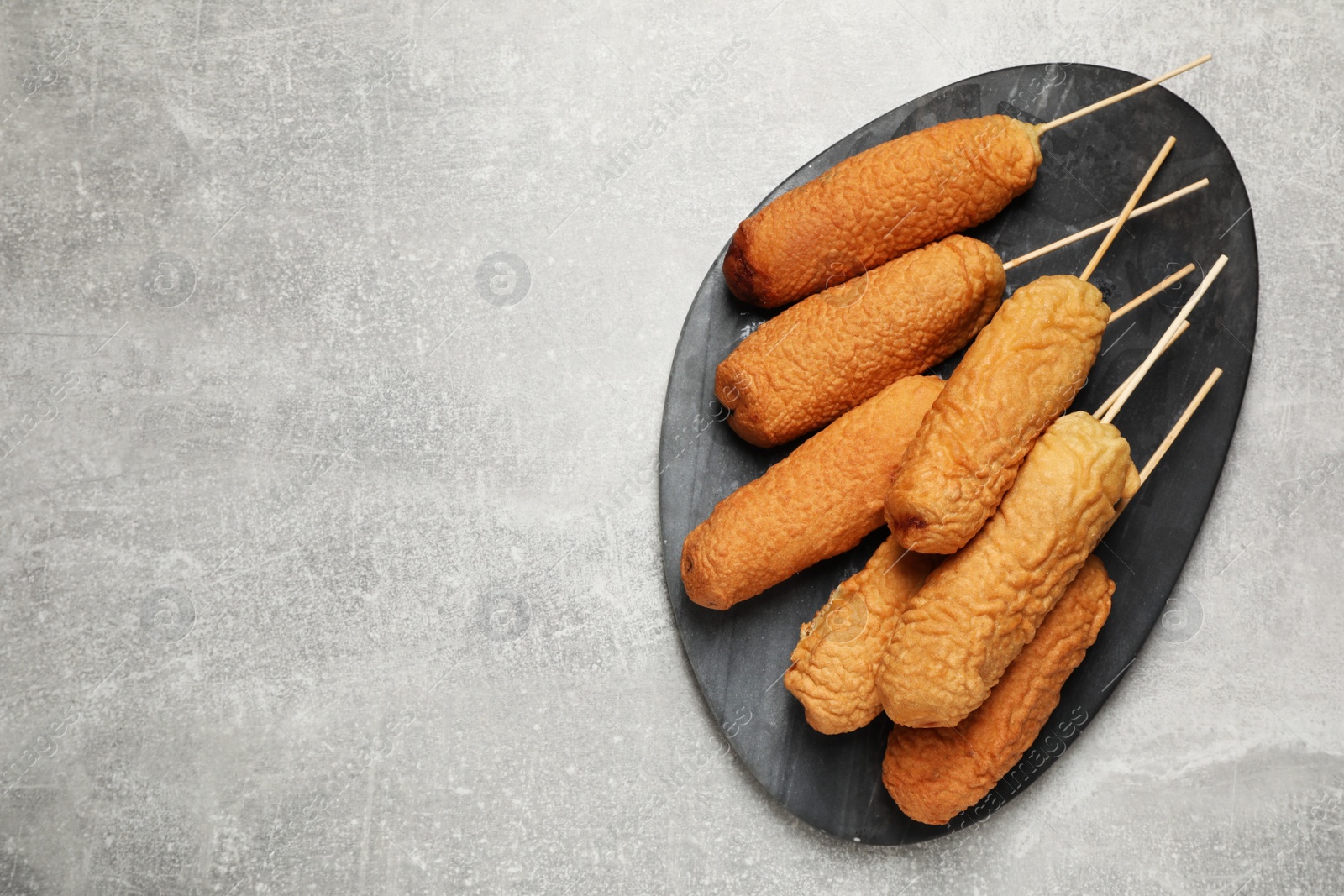 Photo of Delicious deep fried corn dogs with board on light grey table, top view. Space for text
