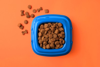 Dry pet food in feeding bowl on orange background, flat lay