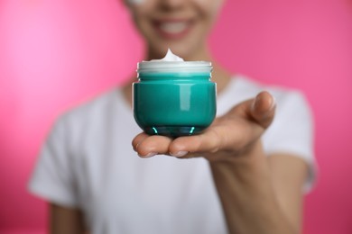 Photo of Woman holding jar of facial cream on pink background, closeup