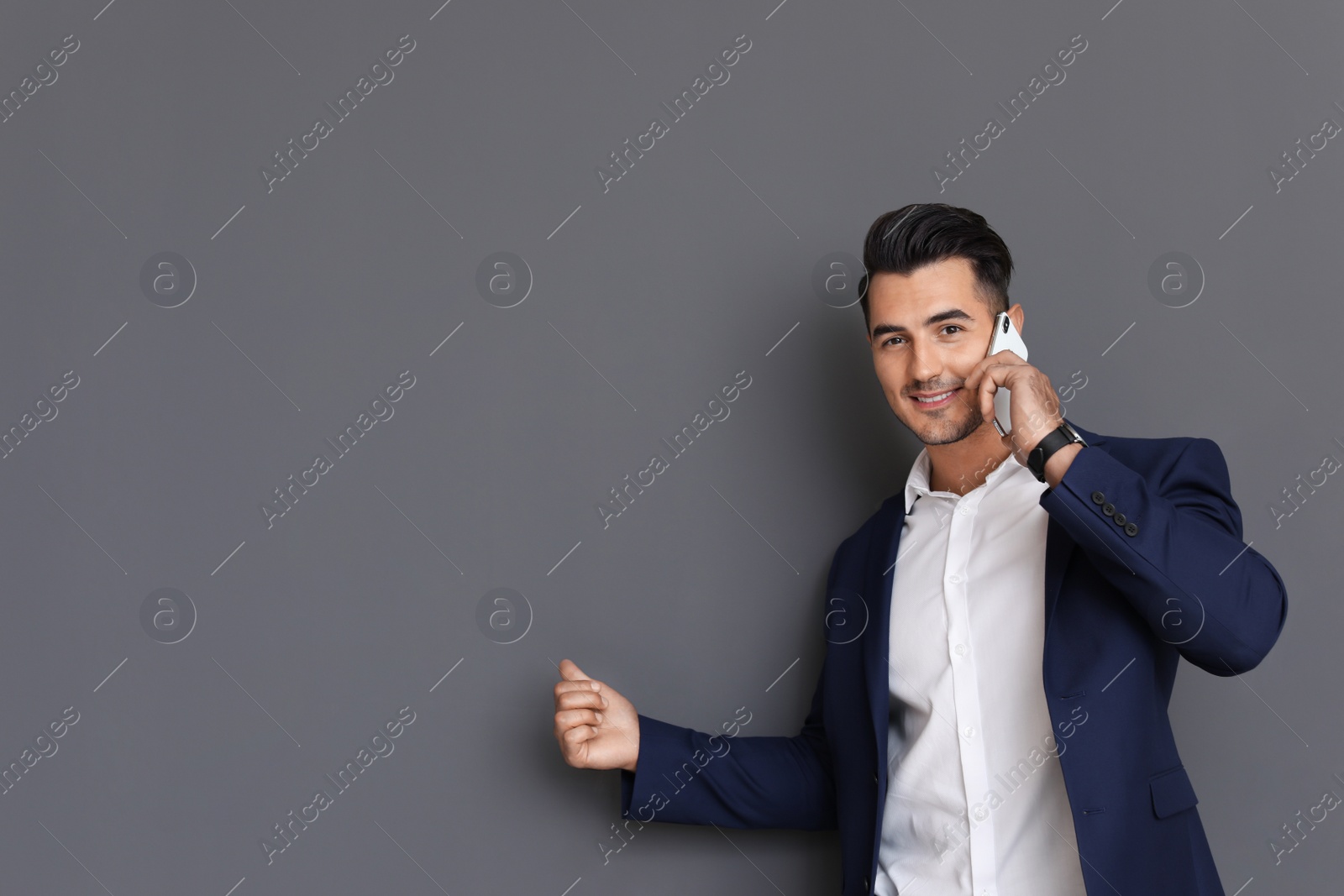 Photo of Handsome young man talking on phone against grey background. Space for text