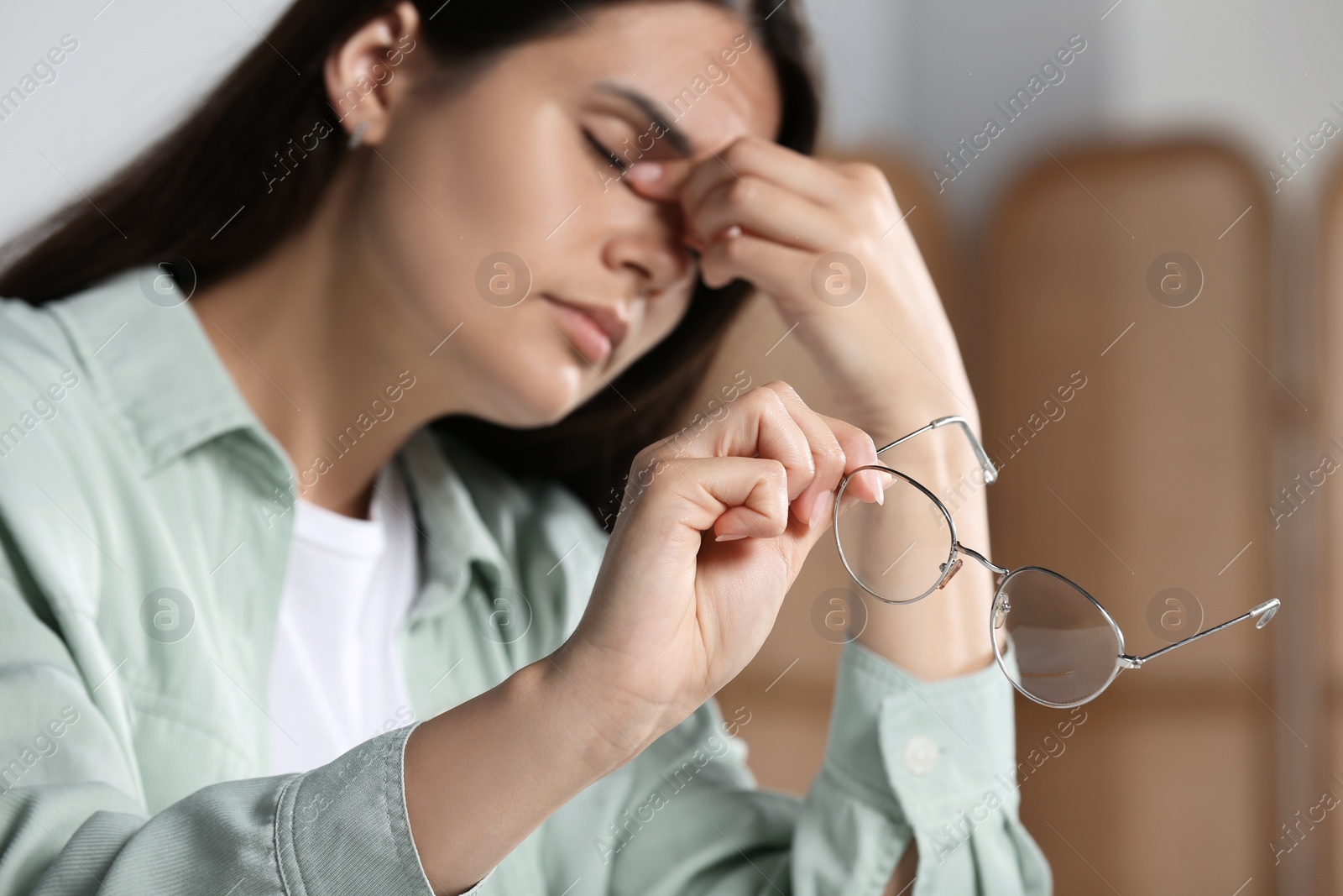 Photo of Young woman suffering from eyestrain in office, focus on hand with glasses