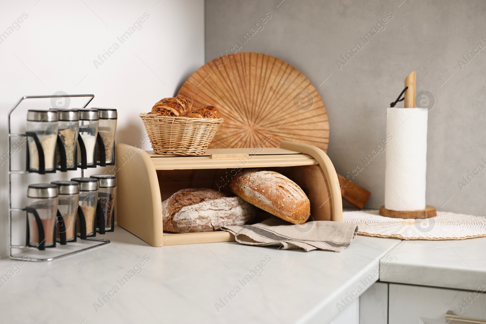 Photo of Wooden bread basket, freshly baked loaves and croissants on white marble table in kitchen